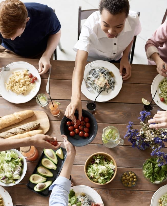 Bird's eye view of a family at a table eating a meal with many different plates of food on the table.